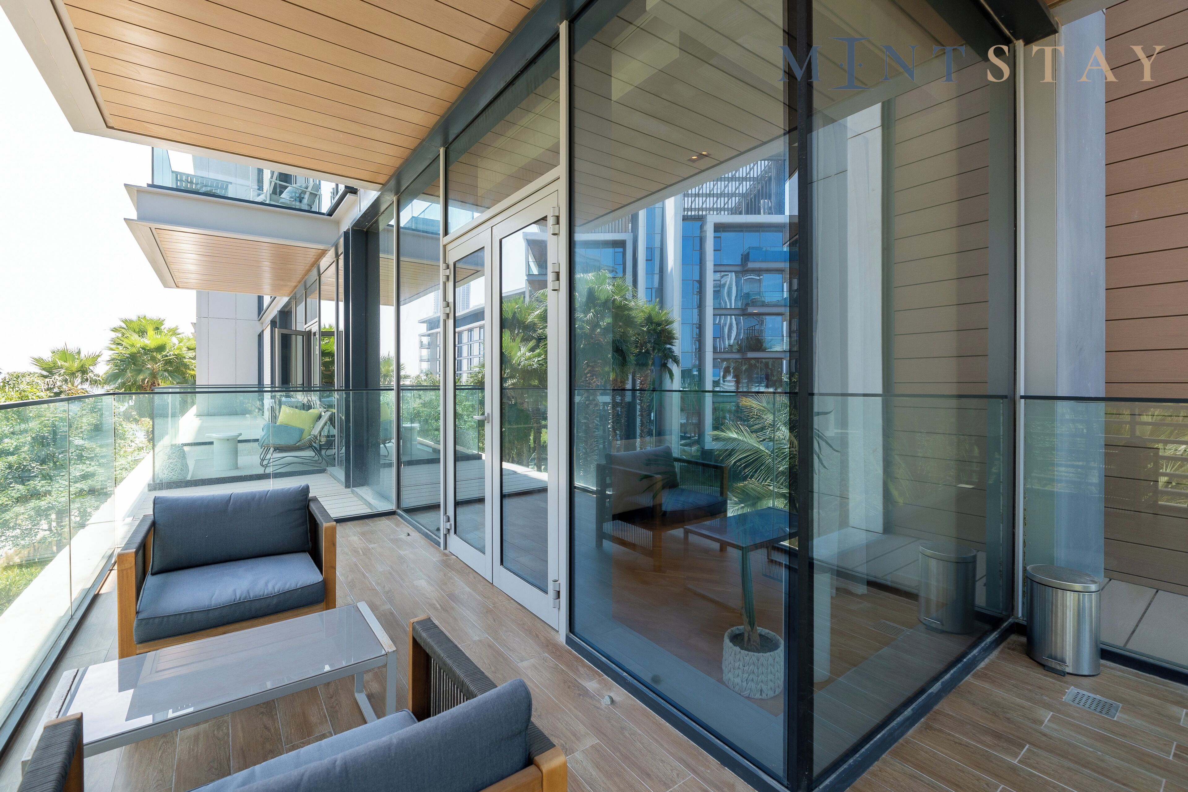Een modern balkon met glazen wanden, houten vloer en buitenmeubilair.