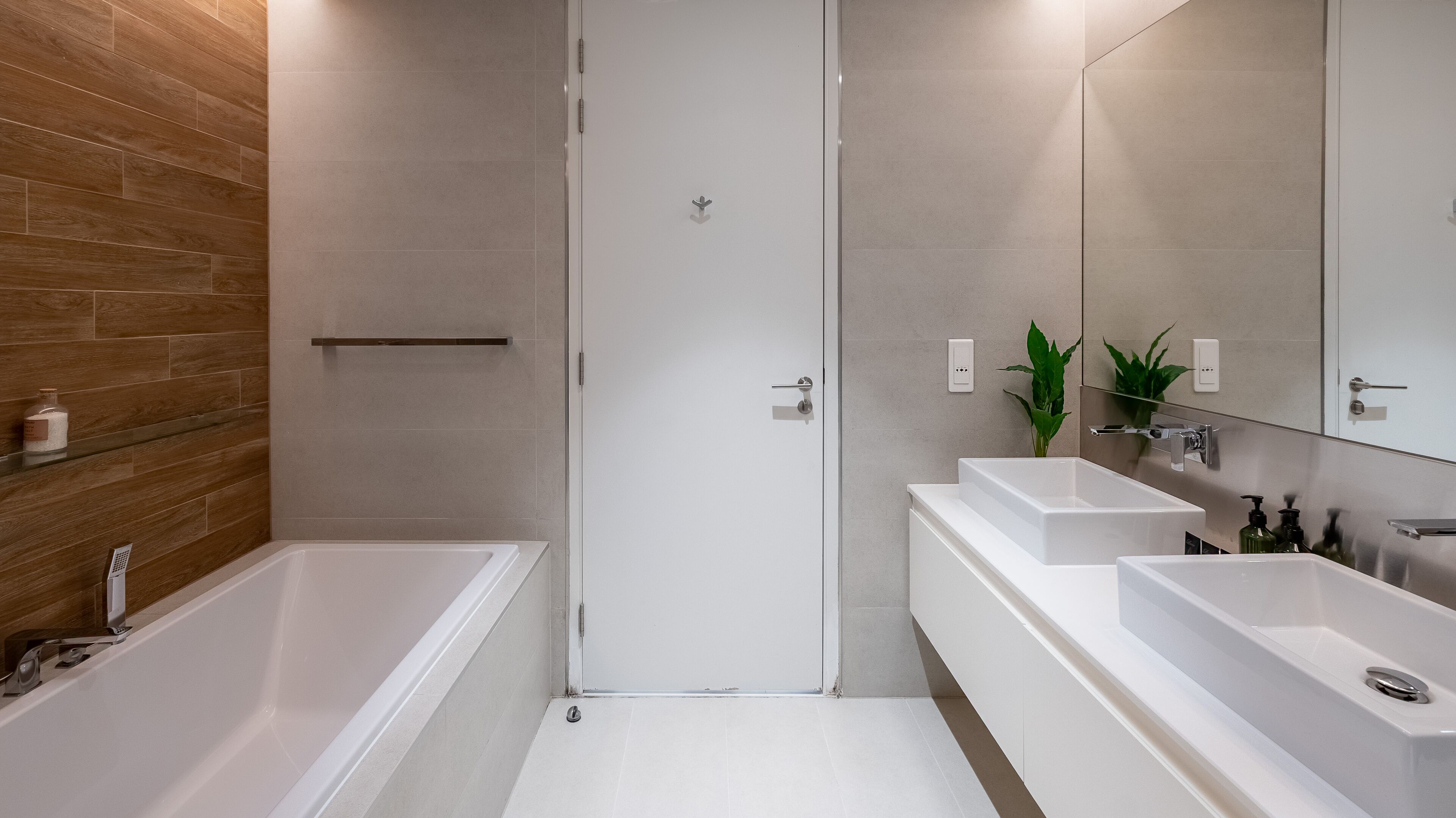 A modern bathroom with a wooden accent wall, a walk-in shower, and a vanity with a mirror and two sinks.