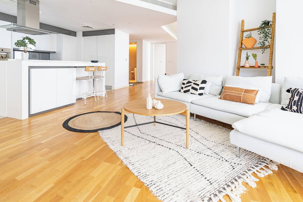 A modern living room with a white sofa, a coffee table, and a kitchen area in the background.