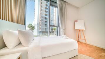 A modern hotel room with a large bed, a bedside table, a whiteboard, and a view of a tall building.