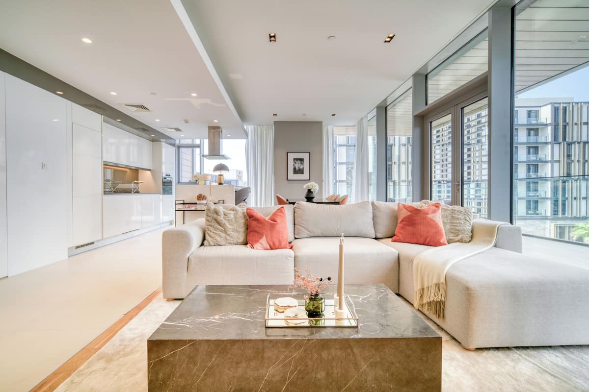 A modern living room with a sectional sofa, a marble coffee table, and large windows offering a view of the city.