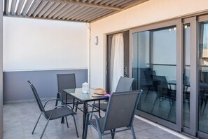 Eine Terrasse im Freien mit Tisch und Stühlen, eine Schiebetür aus Glas und eine Decke mit Lamellen.