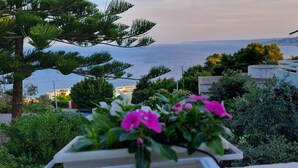 A coastal view with a garden in the foreground, a building with a balcony, and a clear view of the sea.