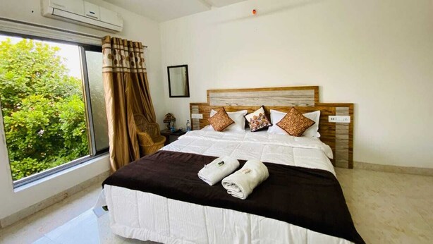 A hotel room with a large bed, a window with curtains, an air conditioning unit, and a ceiling fan. - Payal Palace (Maheshwar)