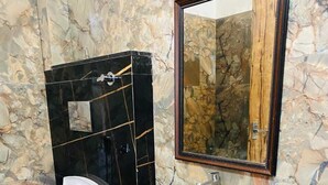 A bathroom with a marble wall, a black vanity with a marble sink, a white toilet, and a mirror with a wooden frame. - Payal Palace (Maheshwar)