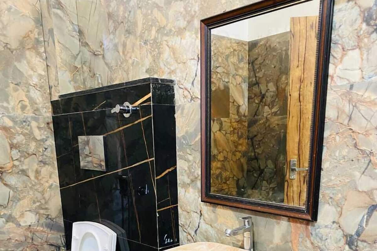 A bathroom with a marble wall, a black vanity with a marble sink, a white toilet, and a mirror with a wooden frame.