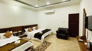 A hotel room with two beds, a sofa, a TV, and an air conditioning unit. - Payal Palace (Maheshwar)