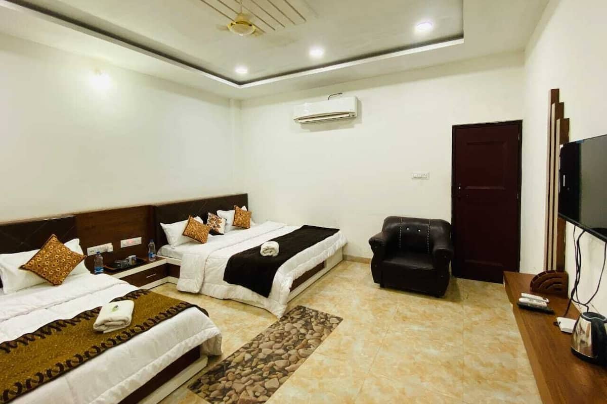 A hotel room with two beds, a sofa, a TV, and an air conditioning unit.