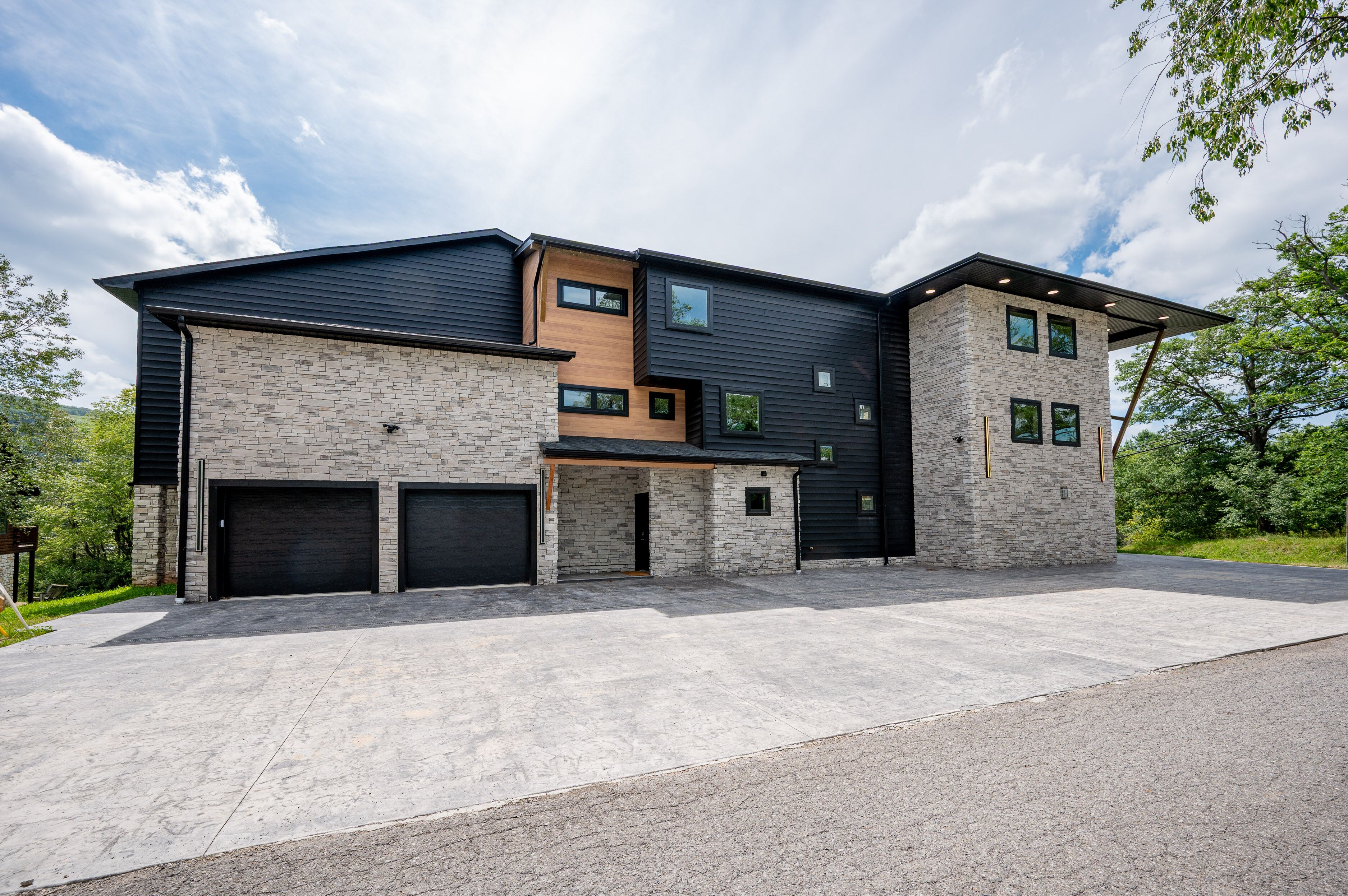 Une maison moderne à deux étages, dotée d’un garage, d’une façade en pierre et d’un toit plat.