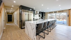 A modern kitchen with a marble island, stainless steel appliances, and a bar seating area. - New! Epic lakefront home with indoor pool! (McHenry)
