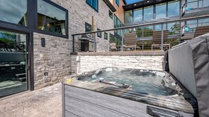 A modern building with a stone facade, large windows, and a hot tub in the foreground. - New! Epic lakefront home with indoor pool! (McHenry)