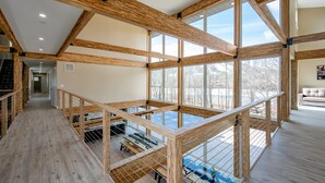 A spacious interior with high ceilings and large windows, wooden beams, and a mezzanine level with seating. - New! Epic lakefront home with indoor pool! (McHenry)