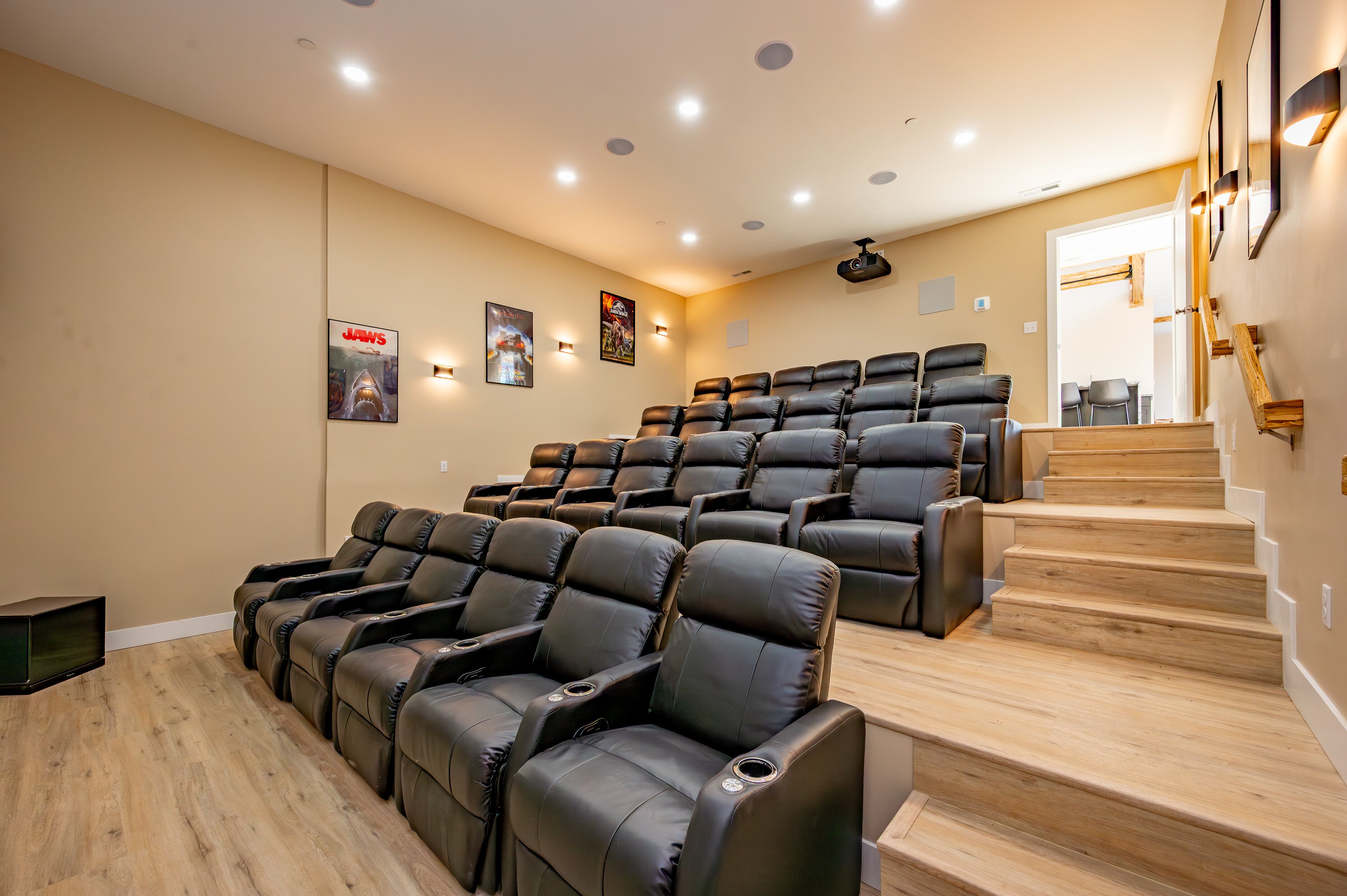 Un cine en casa con varios sillones de cuero negro reclinables, escaleras de madera e iluminación instalada en la pared.