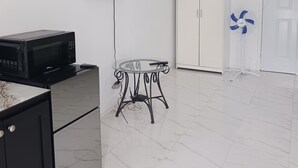 A room with a flat-screen TV mounted on the wall, a white wardrobe, a glass table with a remote control, and a standing fan. - Self Contained Room 3 Tower Isles near Ocho Rios  (Tower Isle)