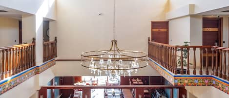 Un hall d’entrée spacieux avec un haut plafond en bois, un lustre central et un coin salon comprenant un canapé et des fauteuils.