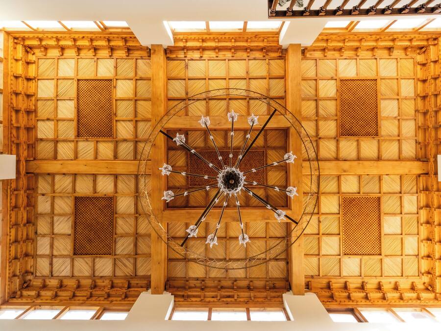 Een kamer met hoge plafonds, een houten spilplafond en een kroonluchter in het midden.