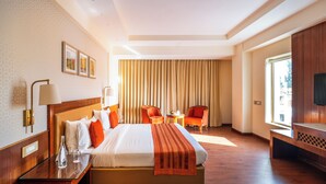 A hotel room with a large bed, two chairs, a TV, and a window with curtains.