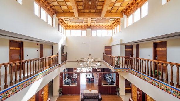 A spacious hotel lobby with a high ceiling, wooden railings, and a central chandelier.