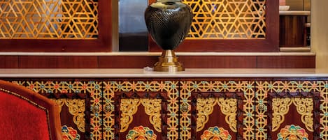 A lobby with a patterned wooden partition, a red upholstered chair, and a table lamp.
