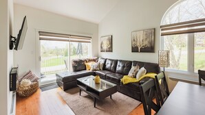 A modern living room with a sectional sofa, a glass coffee table, and a dining table. - Cozy and close to beach ,3 bedroom condo in Magog (Magog)