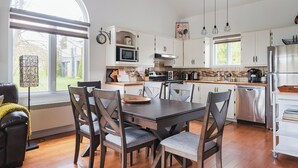 A modern kitchen with white cabinets, a dining table with chairs, a large window, and a view of the outdoors. - Cozy and close to beach ,3 bedroom condo in Magog (Magog)