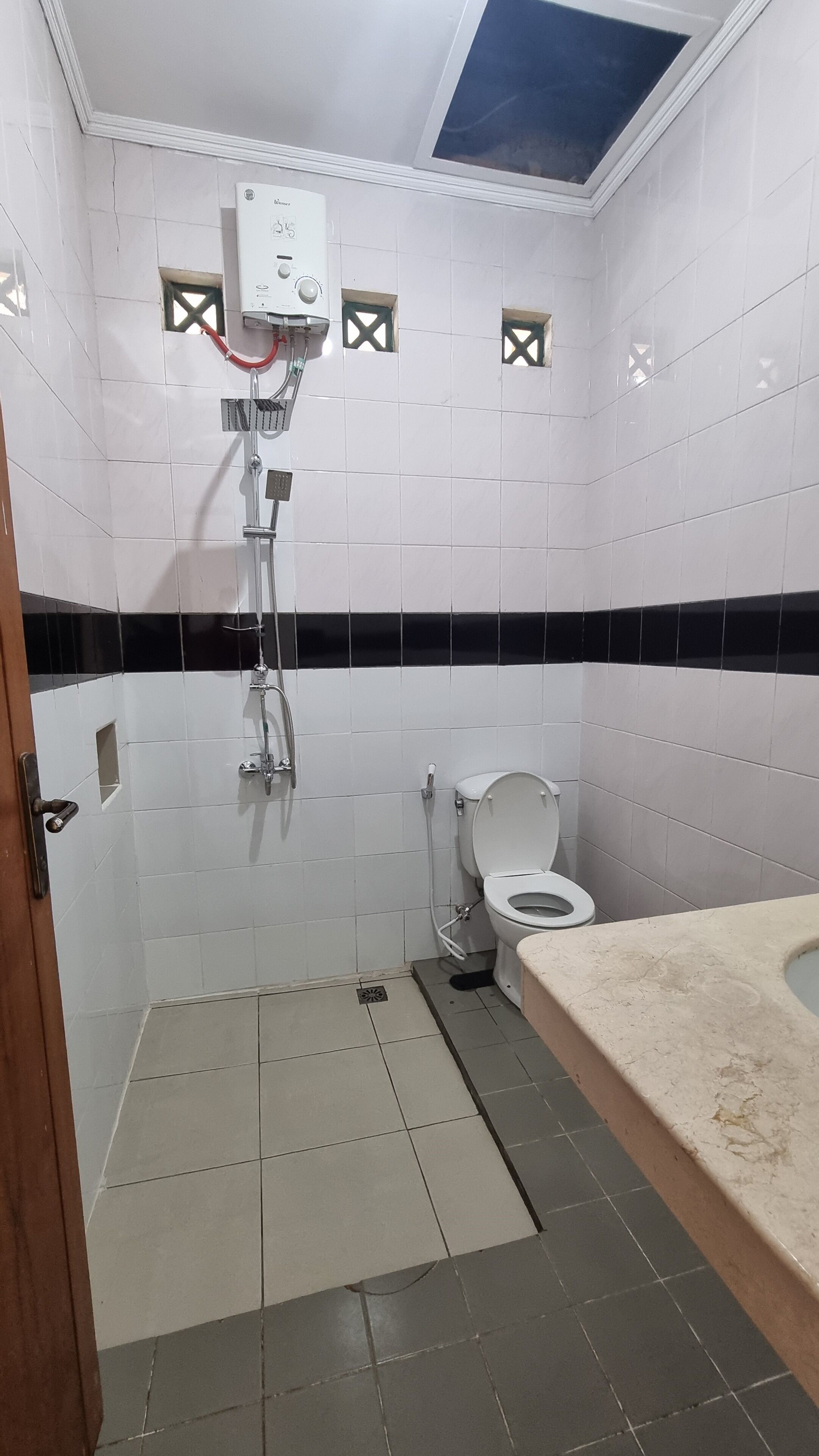 Un bagno con piastrelle bianche, uno schienale a righe bianco e nero, una doccia, un WC e un lavandino.