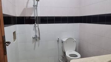 Un bagno con piastrelle bianche, uno schienale a righe bianco e nero, una doccia, un WC e un lavandino.