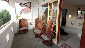 Ein überdachter Balkon mit Steinböden, Holzstühle mit aufwendigen Schnitzereien und Blick auf ein Haus mit rotem Ziegeldach.