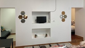 A modern living room with a flat-screen TV mounted on a white wall, surrounded by hexagonal mirrors. There are two small shelves below the TV, each holding a plant. - Cozy Apartment , Casa Para um fim de Semana Para Descobrir a Vila de Elvas (Ajuda, Salvador e Santo Ildefonso)