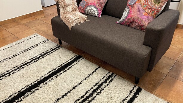 A grey sofa with patterned cushions, a beige throw blanket, and a striped rug in a living room with tiled flooring. - Cozy Apartment , Casa Para um fim de Semana Para Descobrir a Vila de Elvas (Ajuda, Salvador e Santo Ildefonso)