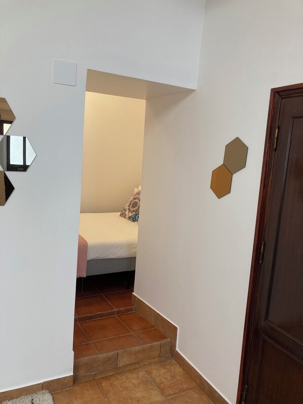A narrow hallway with a bed at the end, a wooden door, and geometric wall decorations.