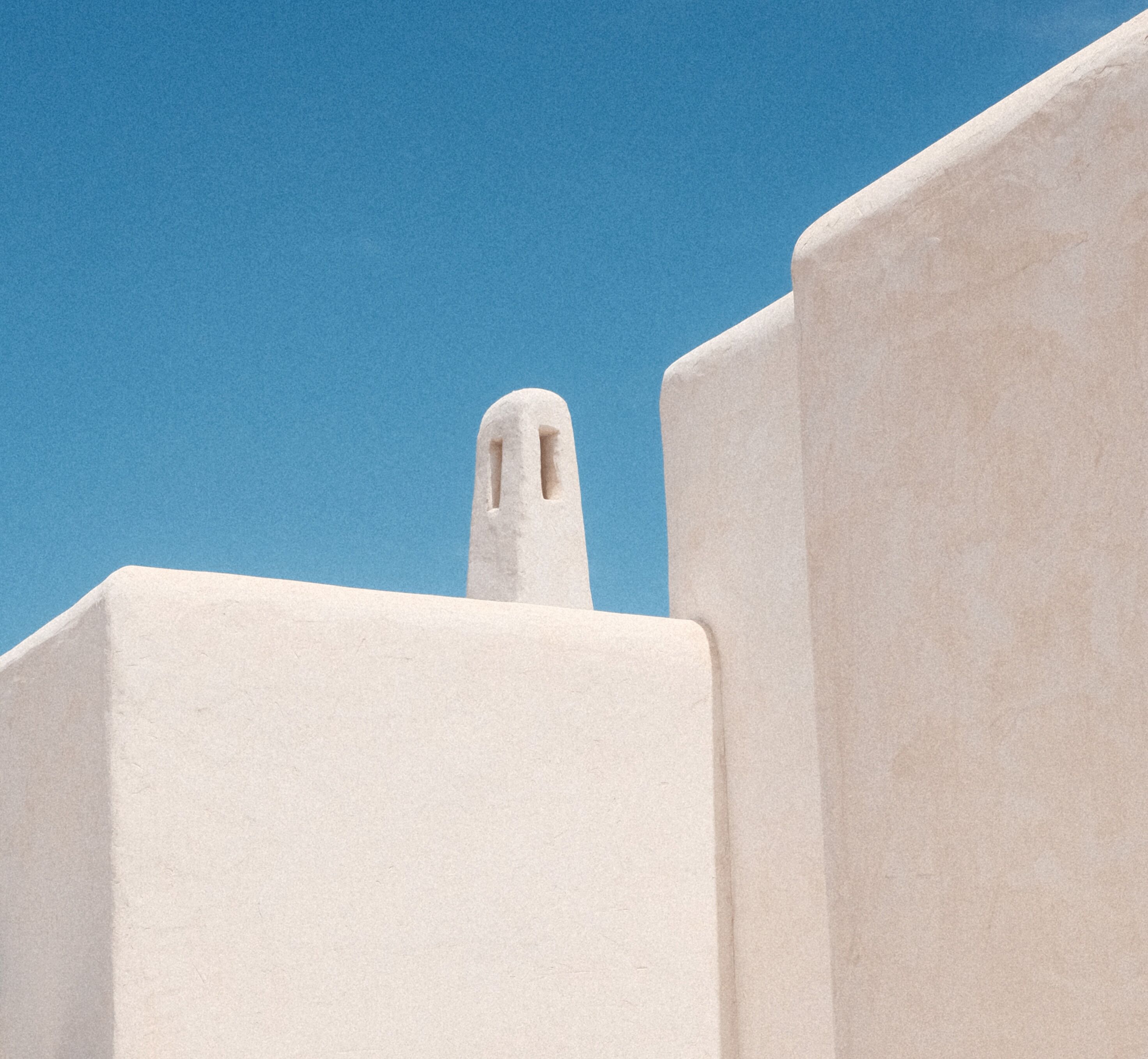 Un edificio blanco con una chimenea destacada contra un cielo azul despejado.