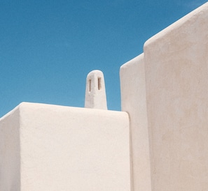 A white building with a prominent chimney against a clear blue sky. - EQUILICUÁ (Carboneras)