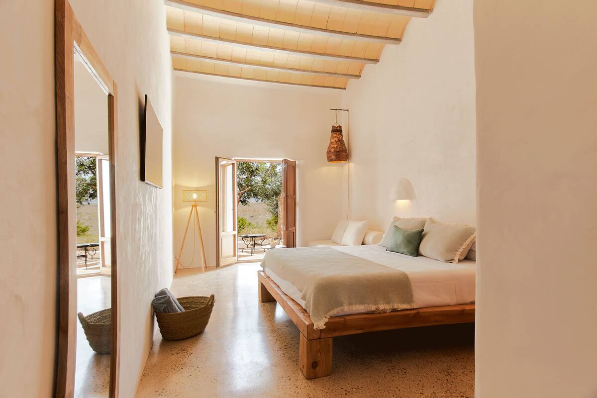 Quarto com cama de madeira, uma janela grande e vista para o exterior.