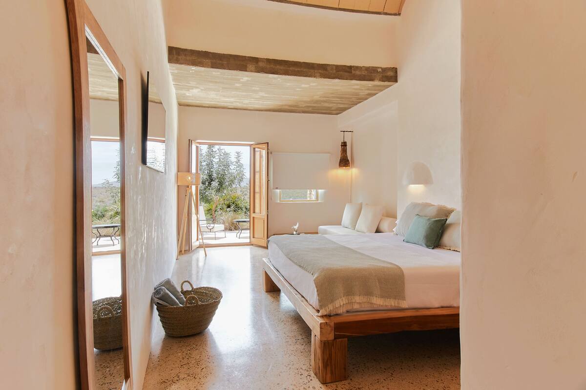 Quarto com cama de madeira, uma janela grande e vista para o exterior.