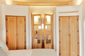 A bedroom with a bed, wooden wardrobe, and a bathroom visible through a glass door. - EQUILICUÁ (Carboneras)