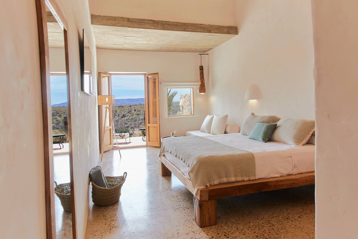 Quarto com uma cama grande, vista através de uma porta aberta e teto rústico.