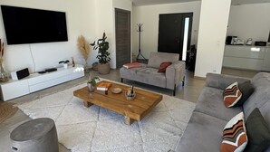 A modern living room with a grey sofa, a wooden coffee table, and a flat-screen TV mounted on the wall.