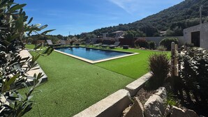 A swimming pool surrounded by artificial grass, with a mountain backdrop and a clear sky.