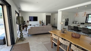 A spacious living area with a large sofa, dining table, and kitchen in the background.