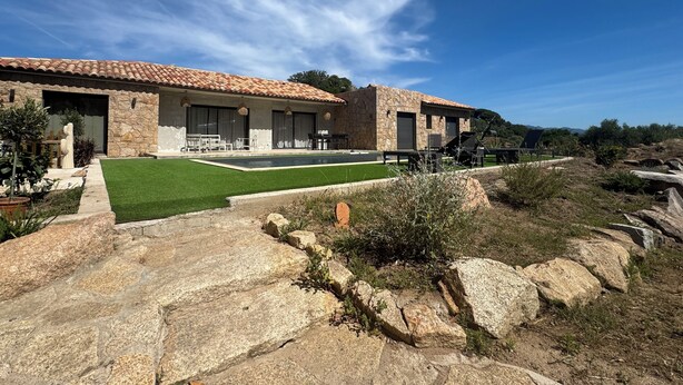 A modern house with a stone facade, a swimming pool, and a well-maintained lawn.