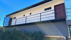 Een gebouw met twee verdiepingen, een balkon, een bruine deur en een raam.