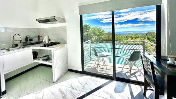Een moderne keuken met een groot raam dat uitkijkt op een balkon met stoelen.