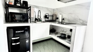 Een kleine keuken met een inbouwmagnetron, een koffiezetapparaat, een spoelbak en een compacte koelkast.