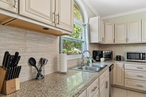 Una cocina con encimeras de granito, armarios blancos, electrodomésticos de acero inoxidable y un ventanal que proporciona luz natural.