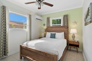 A bedroom with a wooden bed, a ceiling fan, a nightstand with a lamp, and a window with curtains.