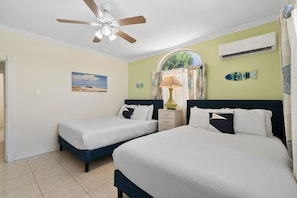 Habitació d'hotel amb dos llits, ventilador de sostre, aire condicionat, decoració de paret amb tema de platja i finestra amb cortines.