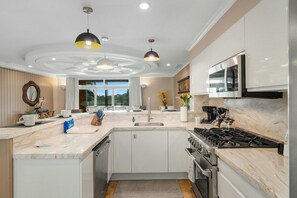 Cocina moderna con una isla central, electrodomésticos integrados, iluminación colgante y vistas a través de un ventanal.