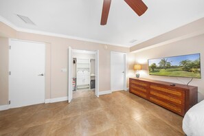A bedroom with a bed, a TV, a wooden dresser, a closet, and a ceiling fan. - Ground-level 4BR Lake View Condo, Walk to Beach (Noord)