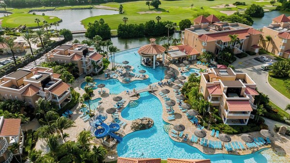 A resort with multiple swimming pools, a golf course, and a large building with a red roof.